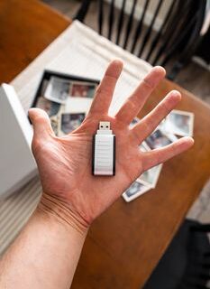A hand holding a USB drive with scattered vintage family photos in the background.