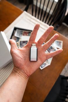 A hand holding a USB drive with scattered vintage family photos in the background.